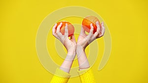 Slim female hands holding tangerines moving at yellow background. Unrecognizable Caucasian woman showing healthful tasty