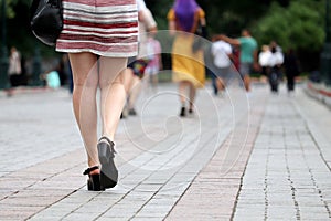 Slim female legs in black shoes, girl in summer dress walking on a city street
