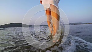 Slim female legs stepping at seaside surf.