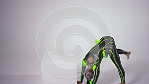 Slim fit flexible young woman standing on hands upside down moving legs. Caucasian performer in bright black and green