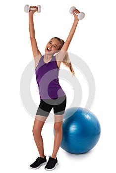 Slim and fit teen girl holding a dumbbells with arms up. Swiss blue ball on background. Full length shot on white