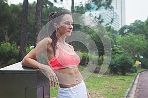 Slim fitness brunette woman with six pack abs wearing pink sport bra standing in city park relaxing after workout