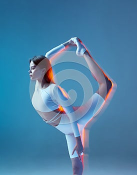 Slim flexible young girl gymnast stretching her leg up, bending lower back. Yoga, pilates workout. Long exposure