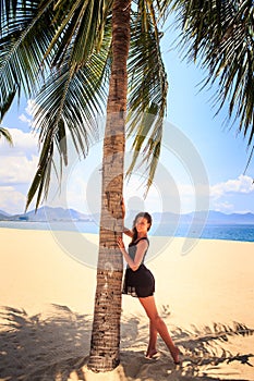 slim girl in black lace frock barefoot touches palm on beach