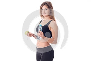 Slim girl in a black top and tights stands sideways holds in one hand apple water
