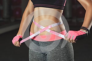 Slim girl bodybuilder centimeter measuring her waist in a gym.
