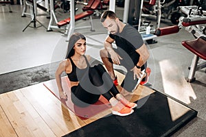 Slim girl dressed in black sports top and tights is doing exercises for the abdominals on the fitness mat in the gym