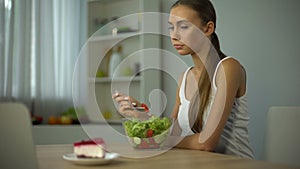 Slim girl eating salad but craving cake, fashion trend to be slender, diet