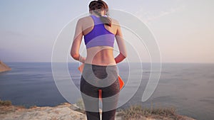 Slim girl goes next to a cliff with a rug for playing sports or yoga. Sunset or dawn by the ocean.