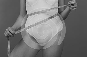 Slim girl holding a centimeter around the waist line. Slim young woman measuring her waist with a tape measure, weight