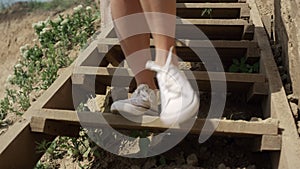 Slim girl legs running down beach staircase wearing white sneakers close up.