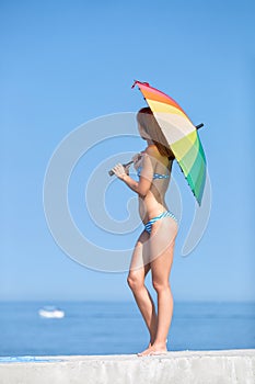 Slim girl with rainbow umbrella on background of sea