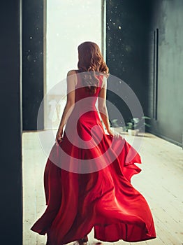 Slim girl with red hair runs into a fashionable room in a loft style with dark black walls and window to the floor