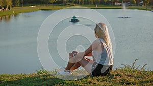 Slim girl sit on hill and looks at beauty of amazing pictorial landscape of European style city with beautiful lake