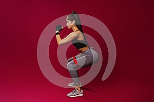 Slim girl in sportswear with elastic bandage doing exercises on a red background with empty side space. The concept of a