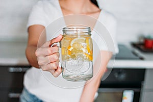 The slim girl young woman holding glass jar with lemon water in kitchen, close up