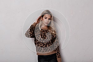 Slim glamorous young woman with long blond curly hair in a stylish leopard sweater in fashionable black leather pants posing