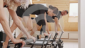 Slim good looking senior woman doing core exercises while taking pilates lesson on a reformer machine, by female