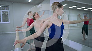 Slim graceful woman moving in fourth ballet position with blurred ballerinas rehearsing simultaneously at background