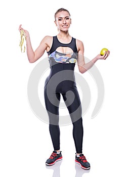 Slim and healthy young woman wearing sportswear tracksuit holding measure tape and green apple isolated on white background.