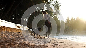 Slim lady walks with playful dog on ocean sandy beach