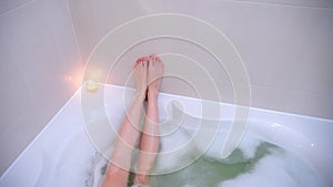 Slim legs of woman on wall lying relaxing in bath with foam in bathroom at home.