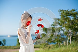 Slim little girl sniffing red flowers outdoors near sea in spring