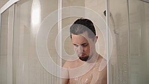 Slim man is lathering his body with soap in a shower, portrait