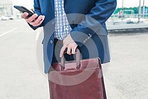 Slim man in a suit tucks his shirt in his pants while calling by phone on the street.