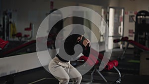 Slim Middle Eastern woman in hijab doing squats in gym indoors. Portrait of motivated fit sportswoman training working