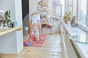 Slim pink haired woman with tattoo on back does forward bend at home training