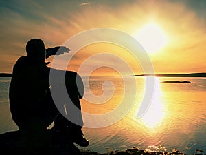 Slim sportsman on rocky coast shadowing eyes and looks into mornning sun above smooth ocean. Marvelous day