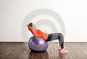 Slim sporty young woman in tight sportswear lying on big fitness rubber ball, stretching and exercising abdomen muscles