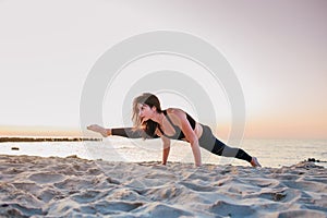 Slim strong young woman in black practicing yoga doing the splits on sand beach close-up with copy space. Sunset, summer. Healhy
