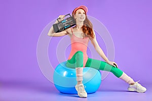 Slim student girl sits on fit ball with portable cassette player waiting to start the retro 80s dance party