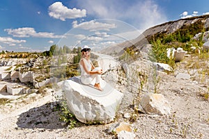 Slim tanned woman sitting on a piece of marble, the mountains, the sky, the dusty road