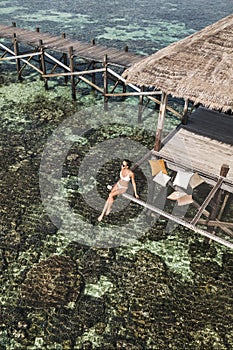 Slim tanned woman in white bikini relaxing in over-reef hammock