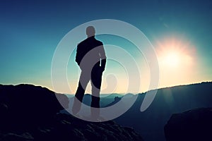 Slim tourist on sharp peak of rocky mountain is watching over misty and foggy morning valley to Sun