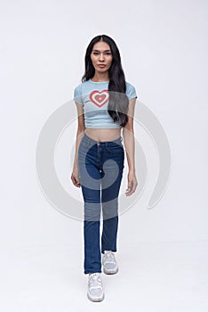 A slim trans woman walking slowly like a model. Sauntering wearing a light blue printed shirt and jeans. Whole body photo on a