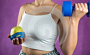 Slim unrecognizable woman with tape measure holding blue dumbbells and apple.