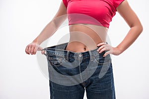 Slim waist of young woman in big jeans showing