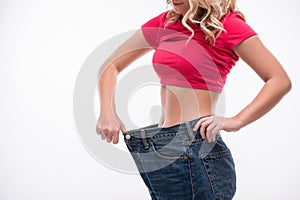 Slim waist of young woman in big jeans showing