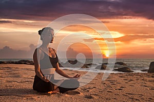 Slim woman does yoga in lotus posture on tropical sea coast or ocean beach outdoors on sunset