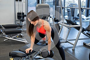 Slim woman exercis with dumbbells on bench at gym
