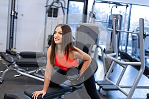 Slim woman exercis with dumbbells on bench at gym