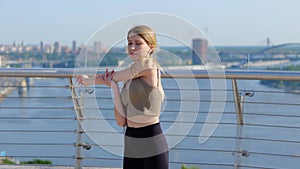 Slim woman having workout outdoors stretching muscles standing outdoor on bridge with view on river. Healthy activity