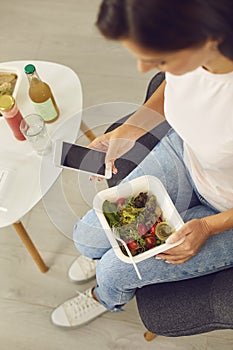 Slim woman holding mobile phone and enjoying healthy low-calorie takeaway vegetable salad