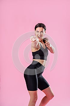 Slim woman kicking the air, with hand and leg up. Athletic girl doing boxing exercises, making a direct kick. Photo of a young