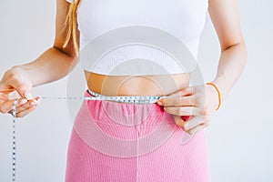 Slim woman measuring her waist`s size with tape measure on white background. Successful weight loss. Slim fit concept