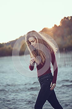 slim woman with messy long hair wearing black jeans and red shirt walking on windy autumn day outdoor on beach